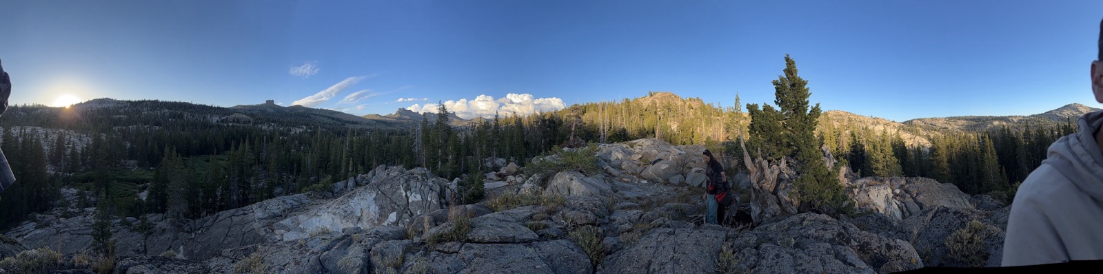 Panoramic view from camp: the sun setting over granite slabs, pines, and high-country ridges under a clear sky