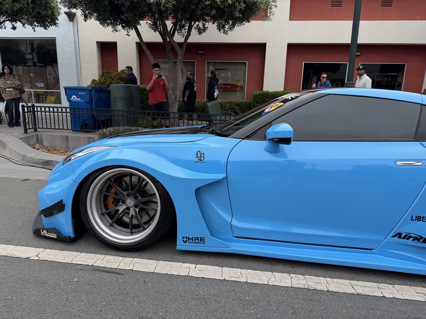 A sky-blue widebody Nissan GT-R parked curbside at Monterey Car Week while onlookers stop to photograph it