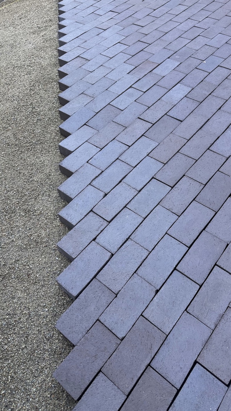 Dark pavers laid in a running-bond pattern beside a gravel patio base